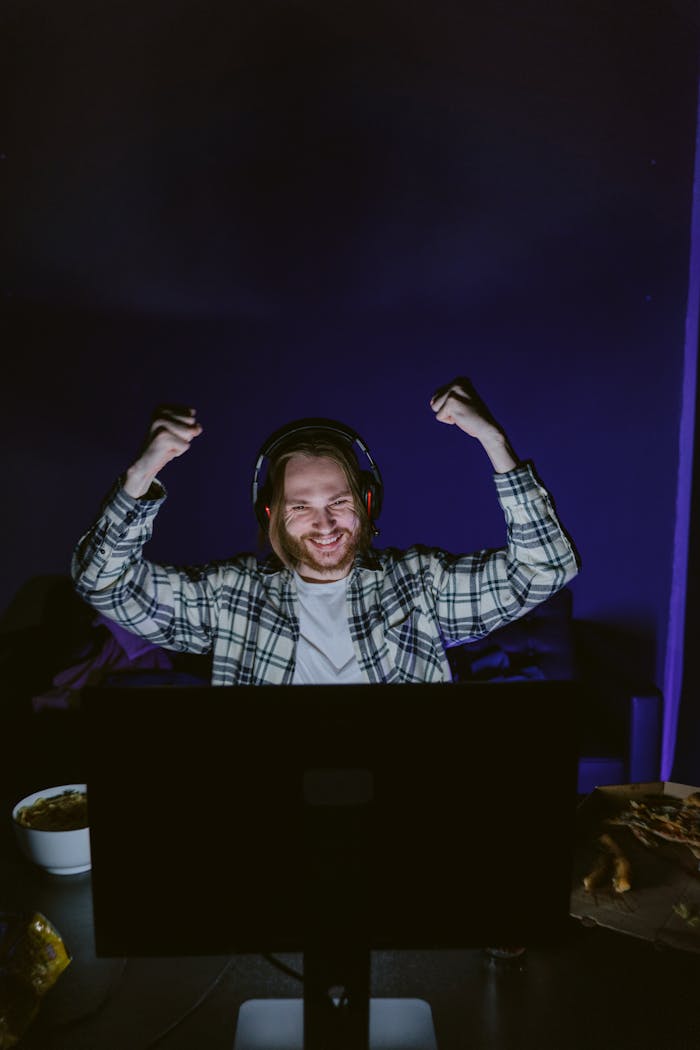 Man with headphones celebrates gaming victory, indoors and happy.